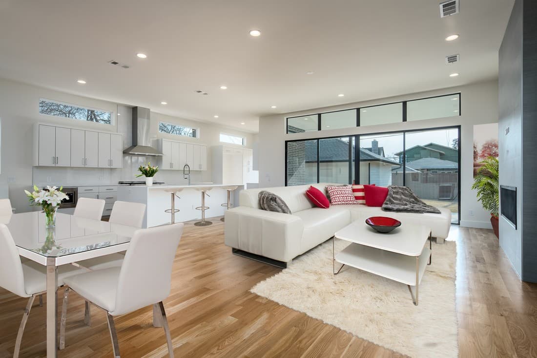 The same open-plan area virtually staged with a light sectional sofa, dining table and chairs, and a soft rug.